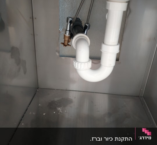 צינור ניקוז לבן מתחת לכיור מתכת